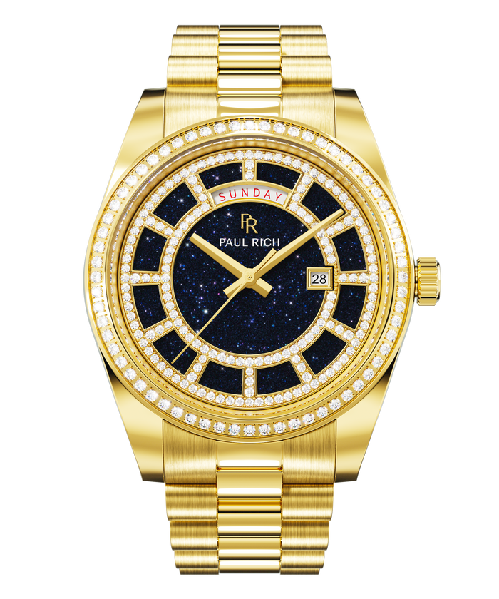 Gold watch with a blue aventurine dial, day and date windows, and a bezel and hour markers set with clear stones on a full gold bracelet.