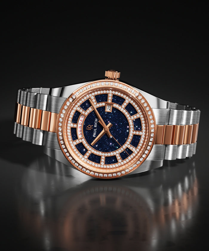 Two-tone silver and rose gold watch with a blue aventurine dial and a pavé stone-set bezel, shown on a steel bracelet against a dark background.