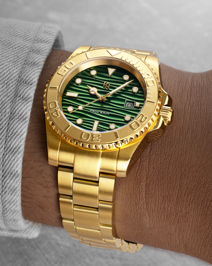 Gold-tone stainless steel watch with a green wave-textured dial shown on a wrist, highlighting the bracelet, bezel, and luminous markers.