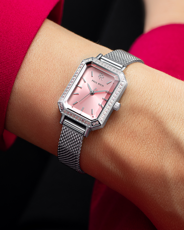 Silver-tone Paul Rich watch with pink sunray dial, pink gem-set octagonal bezel, and silver mesh strap, worn on wrist with a vibrant pink sleeve.