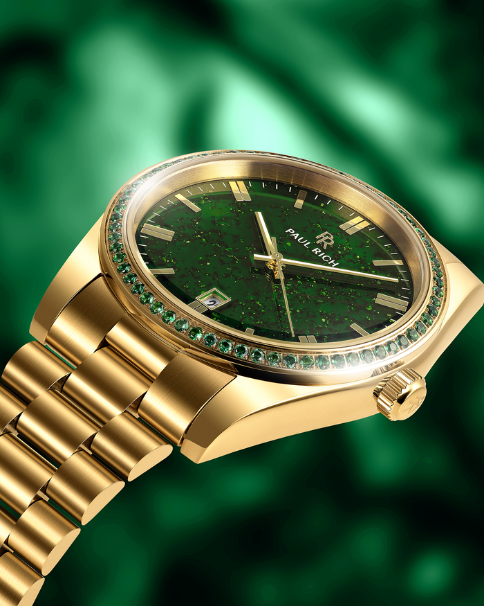 Gold watch with green aventurine dial and green gemstone-set bezel on a gold bracelet, shown at an angle against a green background.