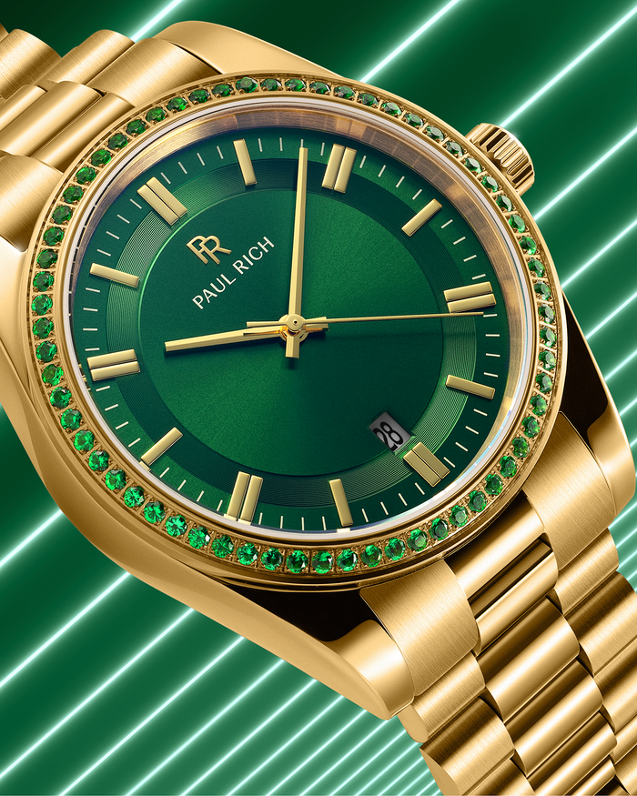 Gold watch with green sunray dial and green gemstone-set bezel on a gold bracelet, displayed against a green background with diagonal light streaks